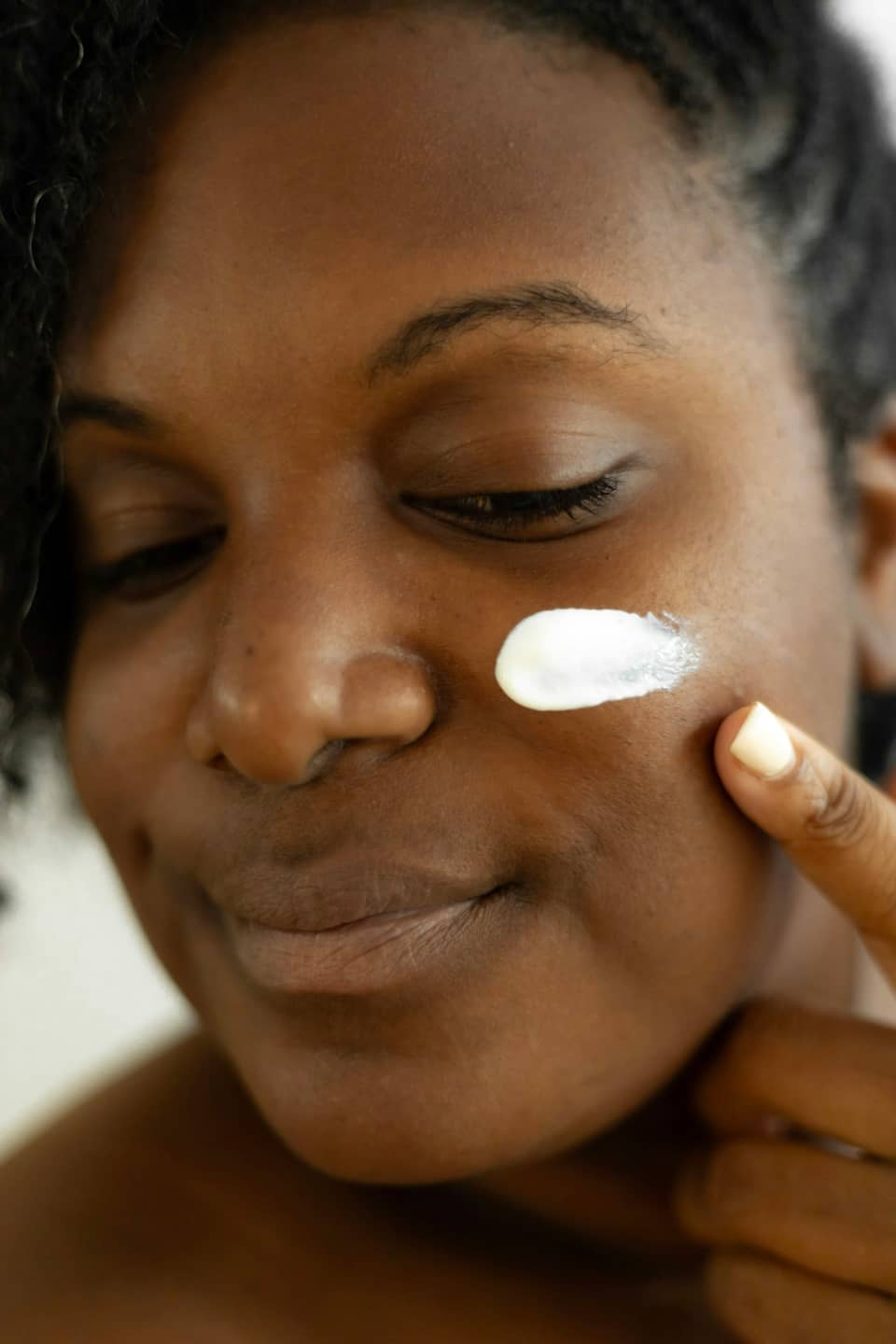 A woman smiling with her eyes closed, a dab of cream on her cheek.