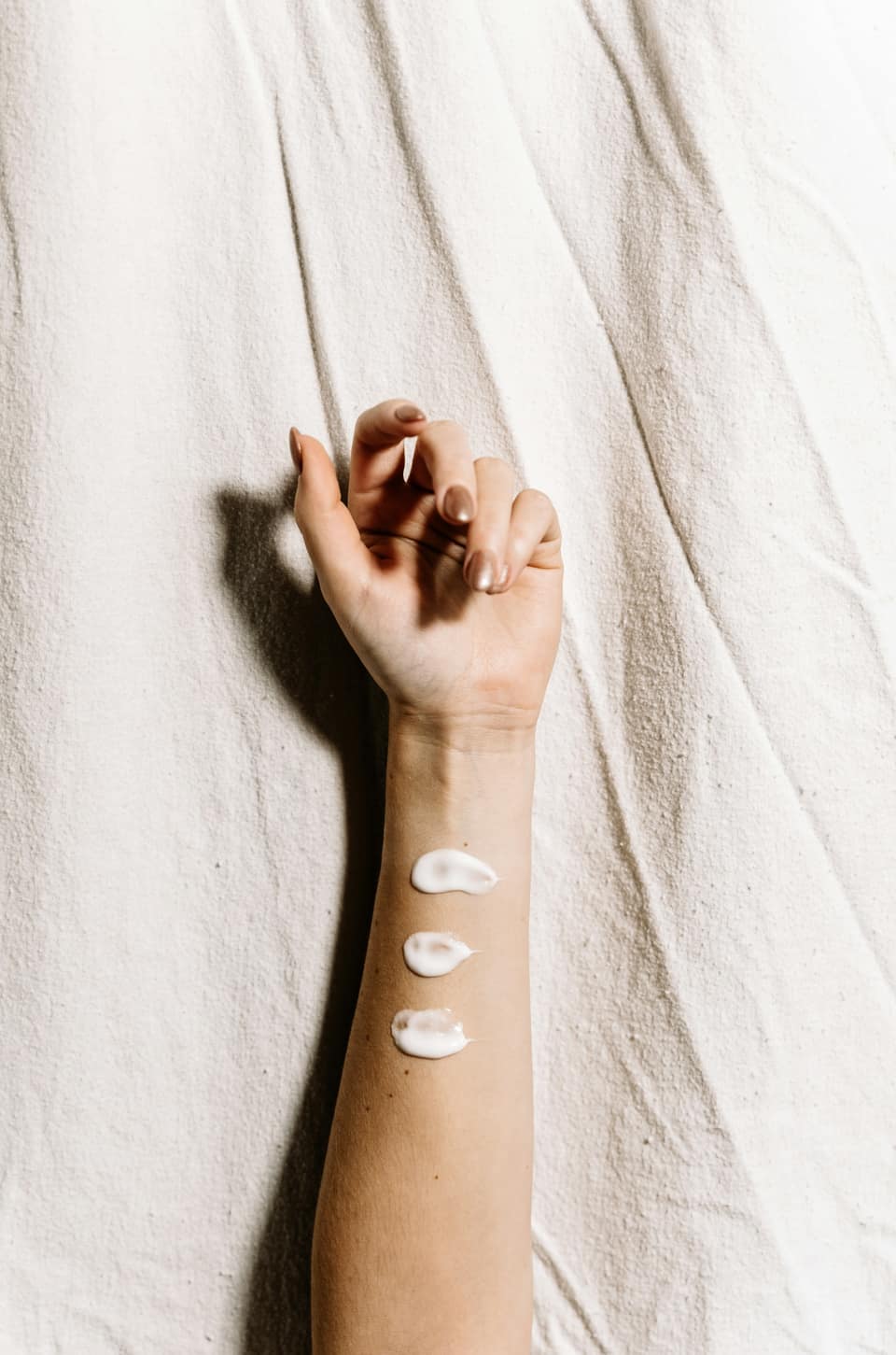 An arm resting on white linen, with three dabs of cream on the inside of the forearm.